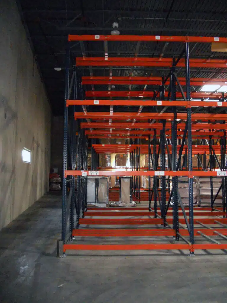 Empty Selective Pallet Rack System with orange bases and blue steel beams in an empty warehouse.