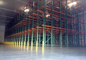 An empty Drive-In Racking and Drive-Through Racking System with green columns and a red base that stretches over 100 feet in a large and empty warehouse.