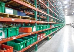 A close up of a row of Selective Pallet Racks with green plastic storage bins on each shelf stretching for 100 feet in a massive warehouse.